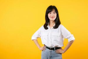 Portrait smiling young asian woman with arms akimbo Happy asia girl posing with arms on hips and looking at camera over yellow background and copy space Confident female get happy and feel relax. photo