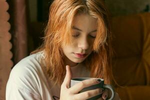 Charming Generation Z Red-Haired Teenager Enjoying Hot Cup by Window photo