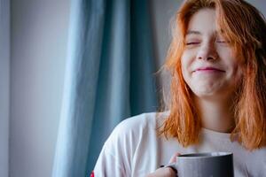 Red-Haired Teenage Girl of Generation Z Enjoying Hot Beverage by Window photo