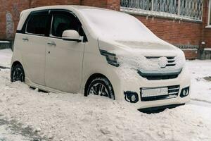 un pequeño coche estacionado en un invierno ciudad calle es ensuciado con sucio nieve desde nieve eliminación equipo foto