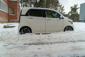 sucio pequeño coche cubierto en nieve escombros estacionado en ciudad calle después nieve eliminación foto