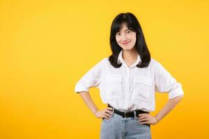 Portrait smiling young asian woman with arms akimbo Happy asia girl posing with arms on hips and looking at camera over yellow background and copy space Confident female get happy and feel relax. photo