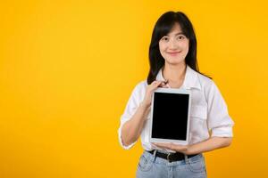 Confident asian woman embraces the digital age, holding tablet on a vibrant yellow background. modern connectivity, tech-savviness, and empowerment. digital lifestyles and technological advancements. photo