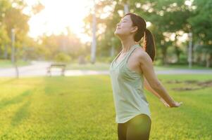 Female jogger. Fit young Asian woman with green sportswear breathing fresh air in park before running and enjoying a healthy outdoor. Fitness runner girl in public park. Wellness being concept photo