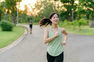 Fit Asian young woman jogging in park smiling happy running and enjoying a healthy outdoor lifestyle. Female jogger. Fitness runner girl in public park. healthy lifestyle and wellness being concept photo