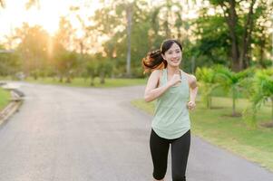 Fit Asian young woman jogging in park smiling happy running and enjoying a healthy outdoor lifestyle. Female jogger. Fitness runner girl in public park. healthy lifestyle and wellness being concept photo