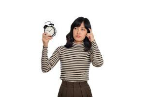 Portrait of thinking young Asian woman with sweater shirt holding alarm clock isolated on white background photo