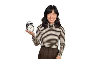 Portrait of excited young Asian woman with sweater shirt holding alarm clock isolated on white background photo