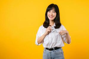 Captivating image of Asian young woman wearing white shirt and denim jeans, confidently holding cash from her shirt pocket. Fashion meets financial empowerment. Perfect for finance and fashion themes. photo