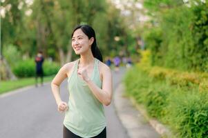 Fit Asian young woman jogging in park smiling happy running and enjoying a healthy outdoor lifestyle. Female jogger. Fitness runner girl in public park. healthy lifestyle and wellness being concept photo