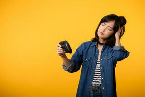 Portrait young asian woman with doubt face wearing denim clothes holding joystick controller and playing video game. Fun and relax hobby entertainment lifestyle concept. photo