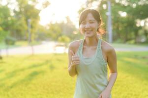 hembra persona que practica jogging. ajuste joven asiático mujer con verde ropa de deporte extensión músculo en parque antes de corriendo y disfrutando un sano exterior. aptitud corredor niña en público parque. bienestar siendo concepto foto