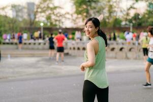 hembra persona que practica jogging. ajuste joven asiático mujer con verde ropa de deporte aeróbicos danza ejercicio en parque y disfrutando un sano exterior. aptitud corredor niña en público parque. bienestar siendo concepto foto