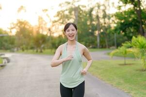 ajuste asiático joven mujer trotar en parque sonriente contento corriendo y disfrutando un sano al aire libre estilo de vida. hembra persona que practica jogging. aptitud corredor niña en público parque. sano estilo de vida y bienestar siendo concepto foto