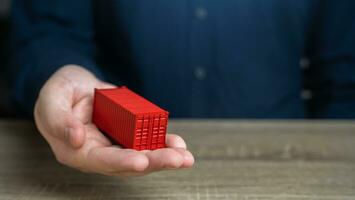 A man holds a red shipping containers in his hand. Cost savings due to bulk purchases or shared shipping expenses. Retailers and Suppliers. Transport operators. Customs authorities. Joint orders. photo