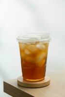 con hielo té en un el plastico taza en un de madera mesa con un blanco antecedentes. foto