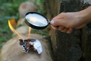 Close up hand hold magnifying glass to make fire for burning paper. Concept, Scicence experiment about convex lens, hold magnifying glass between the sun and tinder. Handy survival skill photo