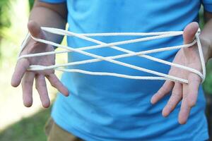 Closeup man hands is playing rope which called cats cradle game. Concept, game involving the creation of various style figures between the fingers. Traditonal playing. photo