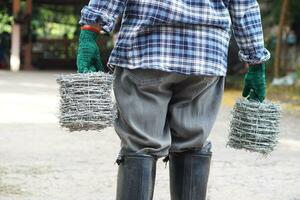 Back view of man worker is carrying rolls of metal barbed wire. Concept, construction tool. Barbed wire is used for make fences , secure property ,make border to show the territory of area. photo