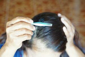 Close up senior woman hand holding tweezers to pluck gray hair from head. Concept, health care. Get rid of gray hair. photo