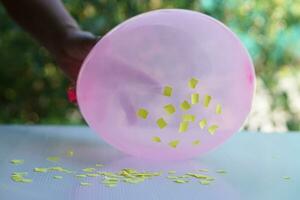 Closeup hand hold pink balloon to do science experiment about static electricity from balloon and pieces of paper. Concept, Science lesson, fun and easy experiment. Education. Teaching aids. photo