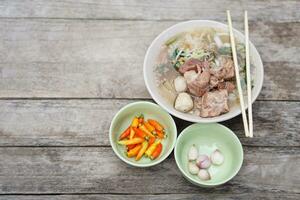 Stewed Pork Soup with meat balls and vegetables in bowl, chopsticks on top, old wooden background. Concept, traditional food. Favorite menu that can cook or order in noodle foodshops in Thailand. photo