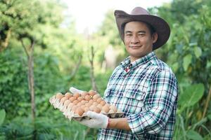 Handsome Asian man farmer holds tray of eggs at garden. Concept, Organic agricultural farming, Farmers produce healthy eco food. Best food during bad economy. Delivery to home. photo