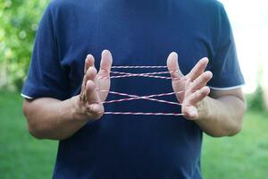 Closeup boy hands is playing rope which called cats cradle game. Concept, game involving the creation of various style figures between the fingers. Traditonal playing. photo