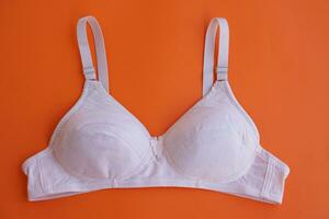 White bra on orange background.Concept, feminine brassiere. Classic comfortable with cup A for female young teenagers. Protect and hold beautiful breasts. Breast cancer awareness. photo