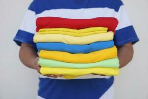 Close up man holds stack of colorful folded clothes after doing laundry. Concept, daily chore, household. Folded clothes for neat and clean. Maintenance and keep garments for sanitary. photo