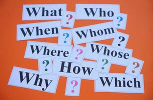 Paper cards with Wh-question words and question marks on orange background. Concept. Teaching aid. Education materials for teach WH- question. Asking questions. Suspicious symbol to find answer. photo