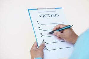 Close up detective hand is writing victims list on paper notepad clipboard. Concept, crime. Analyzing criminal investigation. photo