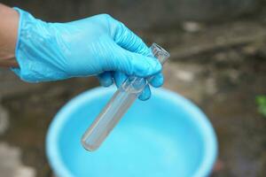 Close up ecologist hand wears glove holds test tube of water. Concept, Inspecting water quality from nature source that use in daily life. Examination water pollution. Environmental problems. photo