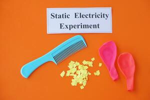 Comb, ballons and small pieces of paper. Equipment, prepared to do experiment about static electricity. Orange background. Concept, Science lesson, fun and easy experiment. Education. Teaching aids. photo