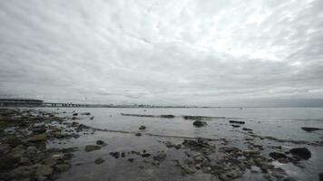 Bottom view of rocky beach and sea in cloudy weather. Action. Beautiful autumn sea with rocky beach and cloudy sky. Rocky beach on background of city on horizon and cloudy sky photo