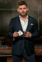 Confident young man with pair of aces and glass of drink in gambling establishment photo