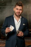 Confident smiling young man with glass of drink and winning two aces in casino photo