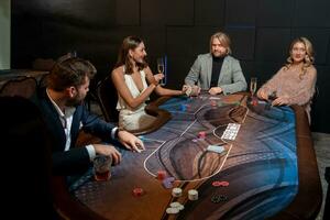 Lucky young woman holding winning set of cards and glass of champagne at poker table photo