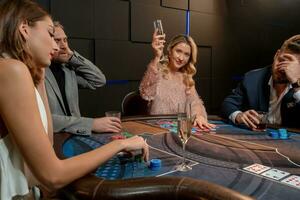 Lucky young blonde raising glass of champagne to successful poker game in casino photo