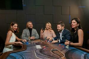 Friendly people drinking alcohol and playing poker at gaming table in casino photo