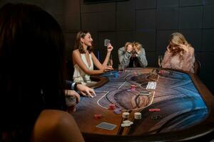 Cheerful girl with winning set of cards and glass of champagne sitting at poker table with upset opponents photo