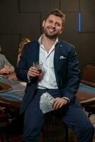 Cheerful young man celebrating victory in poker game with glass of whisky photo