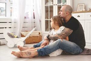 adorable hija vistiendo un blanco vestir con su amoroso padre en un moderno niño habitación con un de madera mueble. contento familia. foto