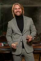 Happy man with pair of aces and glass of whiskey near gaming table in casino photo