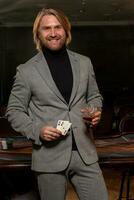 Lucky man standing near gaming table with glass of drink and set of winning pair of aces photo