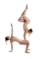 Two flexible girls gymnasts in beige leotards are performing exercises upside down using support and posing isolated on white background. Close-up. photo