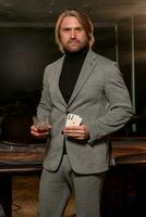 Confident man standing in casino with glass of drink and pair of aces photo