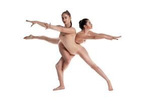 Two flexible girls gymnasts in beige leotards are performing exercises using support and posing isolated on white background. Close-up. photo