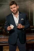 joven póker jugador con vaso de bebida y par de ases en pie en casino foto