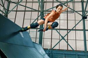 Rollerblader jump high from big air ramp performing trick. Indoors skate park equipment. photo